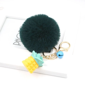 Detail of dark green pompom keychain with yellow resin pineapple and blue bell