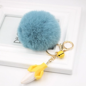 Detailed view of blue plush pompom keychain with golden metal clasp and banana charm