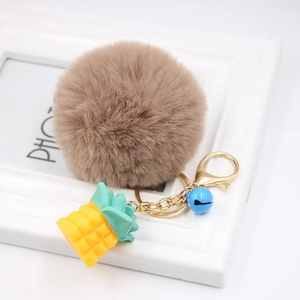 Detail of plush pineapple keychain with brown pom pom, yellow charm and blue bell
