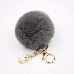 Gros plan du porte-clés pompon gris avec fermoir doré et pendentif licorne