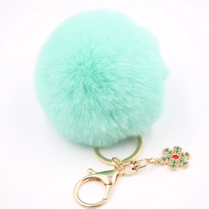 Détail d'un porte-clés pompon en fausse fourrure vert menthe avec fermoir doré et flocon vert