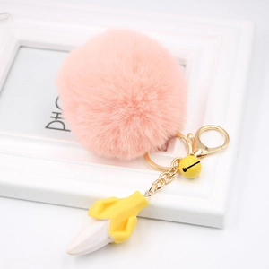 Close-up of pink fluffy pompom keychain with a peeled banana charm and small yellow bell