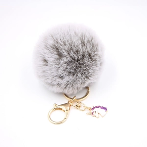 Detailed macro shot of grey fluffy pompom keychain with golden lobster clasp and unicorn charm
