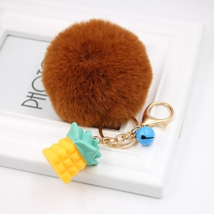 Close-up of fluffy brown faux fur pom pom keychain with golden pineapple charm and blue bell