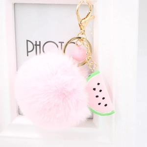 Detailed view of pink pom pom keychain with watermelon charm and golden metal clasp