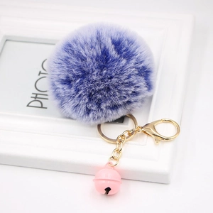 Detail of a fluffy lilac faux fur pompom keychain with a pink bell and golden lobster clasp