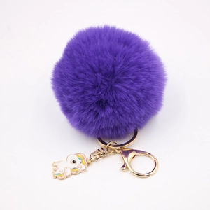 Gros plan d'un porte-clés pompon violet avec clip doré et pendentif licorne