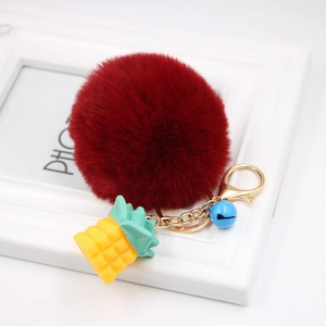 Close-up of fluffy dark red pompom keychain with golden pineapple charm and blue bell