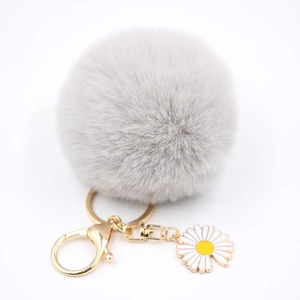 Gros plan du porte-clés pompon en fausse fourrure grise avec breloque marguerite et doré