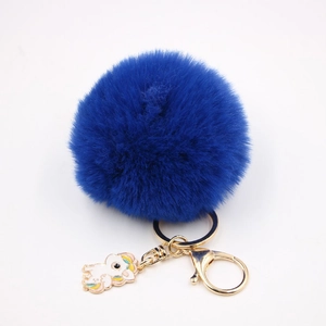 Détail d'un porte-clés pompon bleu roi avec anneau doré et pendentif licorne blanche