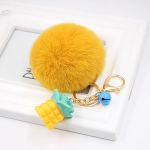 Close-up of yellow faux fur pompom keychain with silicone pineapple and gold metal clasp