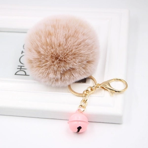 Close-up of fluffy light brown pompom keychain with golden clasp and small pink bell