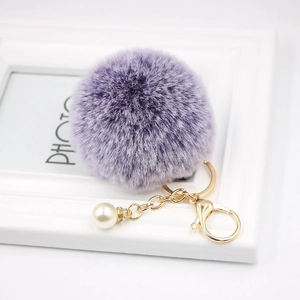 Detail of purple faux fur pompom keychain with white pearl and gold clasp on white frame