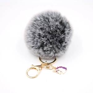 Detail of grey fluffy pompom keychain with golden metal clasp and purple unicorn charm