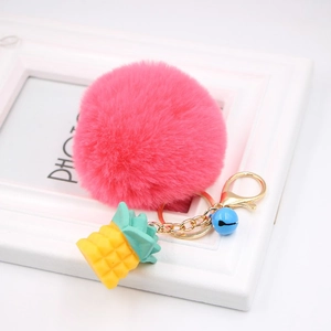 Detailed view of pink faux fur pompom keychain with yellow pineapple and blue bell