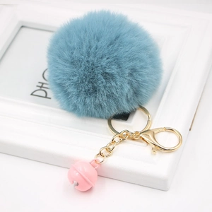 Detail of grey-blue fluffy pom-pom keychain with golden metal chain and pink bell charm