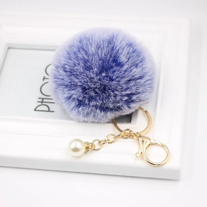 Macro detail of purple faux fur pompom keychain with gold lobster clasp and white pearl charm