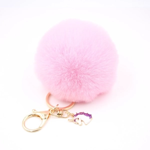 Detailed macro view of pink plush pom pom keychain with gold unicorn enamel charm pendant