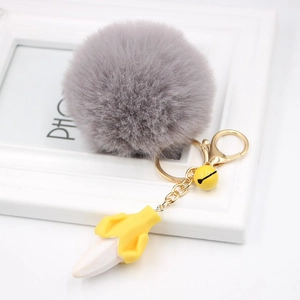 Detail of fluffy grey faux fur ball keychain with yellow banana charm and gold metal hook