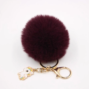 Gros plan d'un porte-clés pompon en fausse fourrure bordeaux avec breloque licorne
