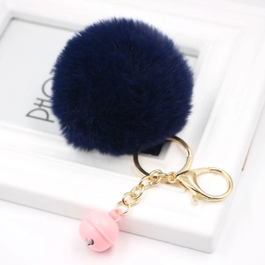 Detail of dark blue plush faux fur keychain with golden lobster clasp and pink bell accent