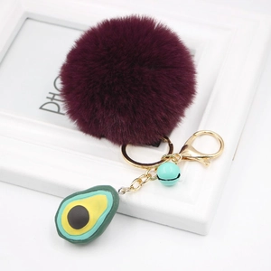 Detail of burgundy plush pom-pom keychain with avocado charm and green bell on gold ring