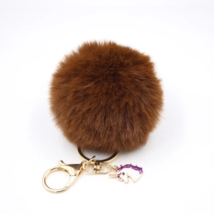 Detail of a brown faux fur pom pom keychain with gold ring and unicorn enamel charm