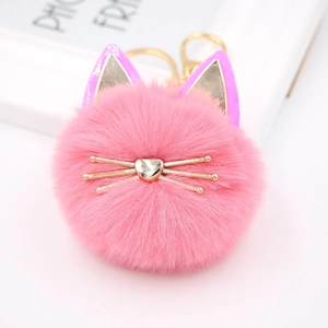 Macro view of pink faux fur cat pompom keychain with golden metal heart nose and whiskers