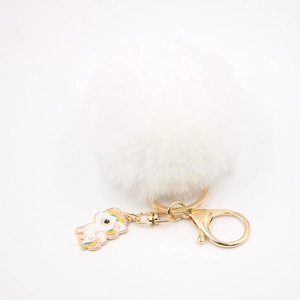 Détail d'un pompon en fausse fourrure blanche avec clip doré et breloque licorne émaillée