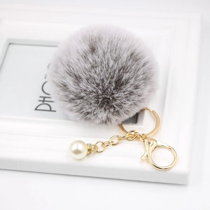 Close-up of fluffy grey pompom keychain with gold chain, lobster clasp and white pearl