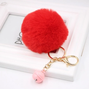 Detail of red faux rabbit fur pom pom with golden lobster clasp and pink bell pendant