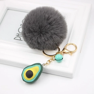 Detail view of avocado keychain with grey faux fur pompom and light green small bell