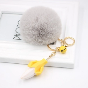 Detail of grey faux fur pom pom keychain with a peeled banana charm and golden metal clasp