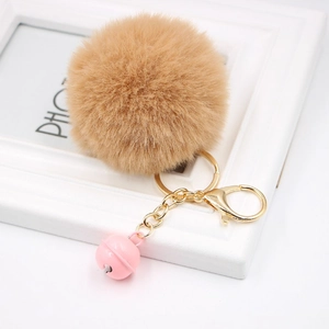 Detail of light brown faux rabbit fur pom pom keychain with gold clasp and pink bell charm