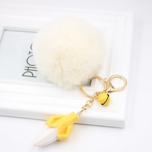 Detail view of plush banana keychain with faux fur ball, golden clasp, and yellow bell