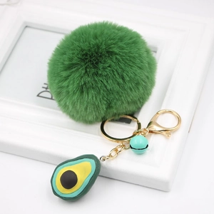 Macro view of fluffy green pompom keychain with 3D avocado charm and gold lobster clasp