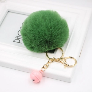 Close-up of fluffy green faux fur pompom with golden keychain and pink bell on white frame