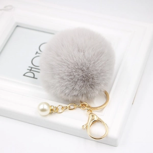 Close-up of grey pom-pom keychain with golden lobster clasp and white faux pearl detail