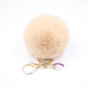 Detailed view of beige fluffy pompom keychain with golden clasp and unicorn enamel charm