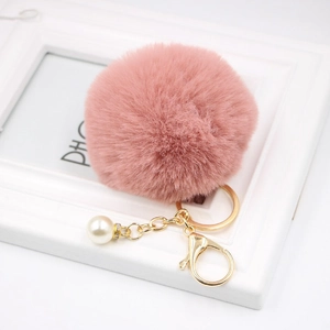 Detail of pink faux fur keychain with gold ring and white pearl charm on a frame
