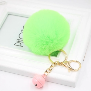 Detail of neon green plush pompom keychain with golden metal lobster clasp and pink bell