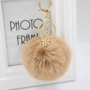 Detail of light brown plush pom pom keychain with gold snowflake pendant and lobster clasp