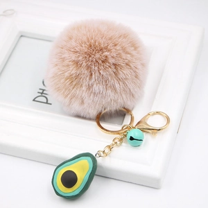 Detail of soft faux fur pom pom and 3D resin avocado charm on golden metal keychain