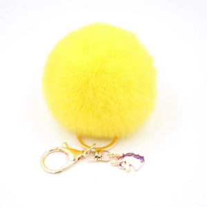 Detail of yellow plush pompom keychain with golden lobster clasp and unicorn charm