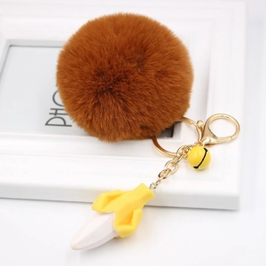 Detail of banana resin pendant with fluffy brown fur ball and golden metal bell keychain