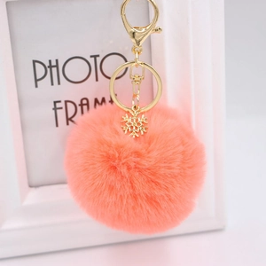 Detail view of coral orange plush ball keychain with golden snowflake charm and hardware
