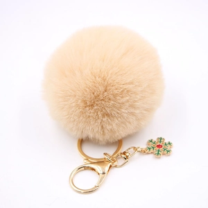 Détail d'un porte-clés pompon beige avec fermoir doré et breloque flocon de neige verte
