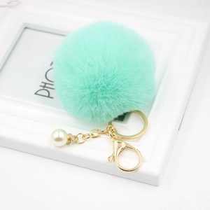 Close-up of mint green faux fur pompom keychain with gold lobster clasp and white pearl charm