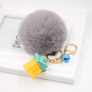 Detail of grey faux fur pompom keychain with pineapple charm and blue bell accent