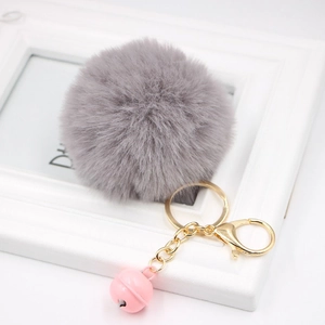 Detail of grey faux fur pom pom with golden metal clasp and pink bell charm
